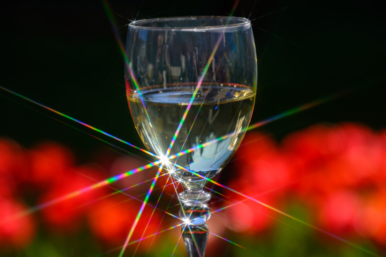 Weinglas mit Weißwein und Regenbogen-Lichtreflexen