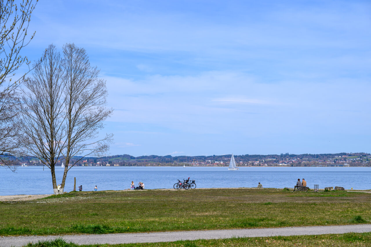 Menschen am See mit Segelboot und Wiese